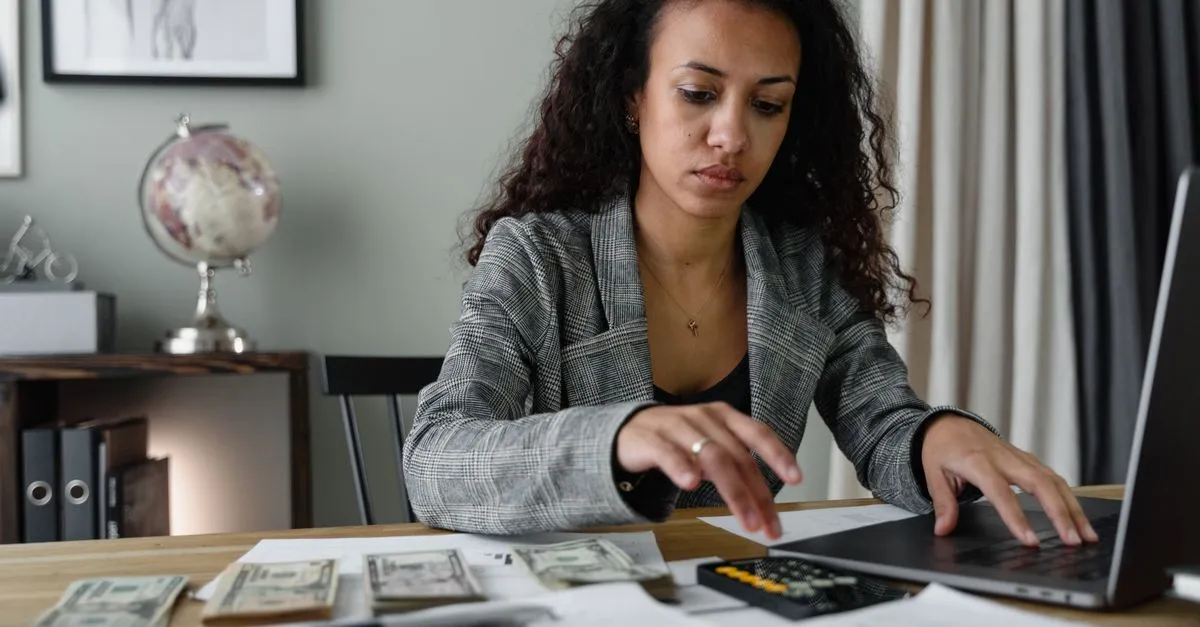 Mujer sumando su dinero con calculadora y laptop en el escritorio