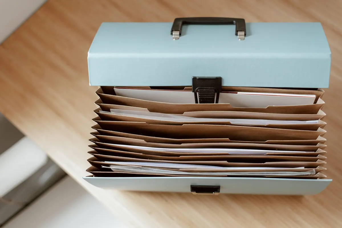 Persona organizando documentos y carpetas sobre una mesa de madera