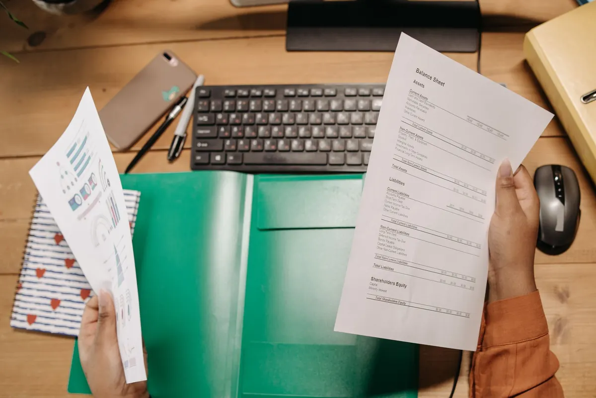 Persona sentada en su escritorio revisando un recibo de nómina impreso junto a una laptop