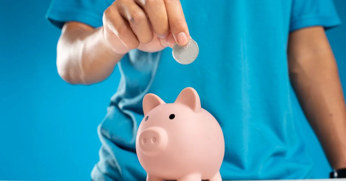 Mano de un niño con monedas y una alcancía