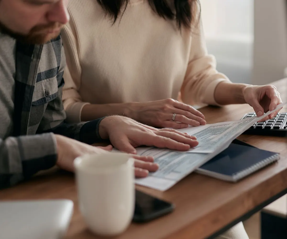 Dos personas revisando documentos bancarios sobre una mesa con una tarjeta y una libreta