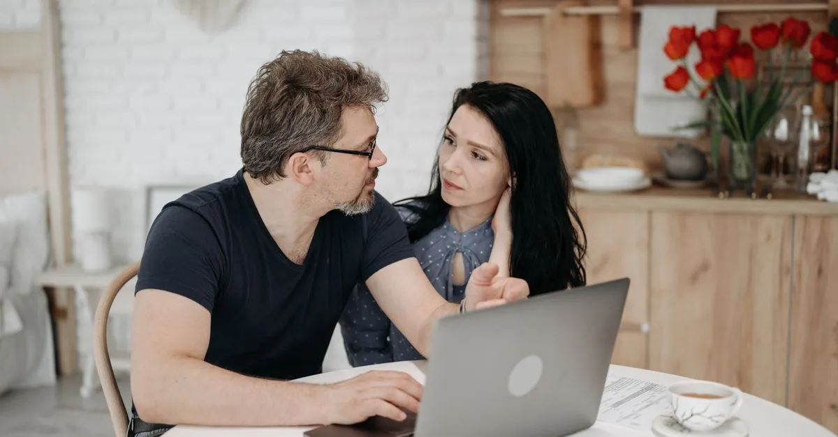 Pareja hablando de dinero frente a una laptop en la mesa de su casa