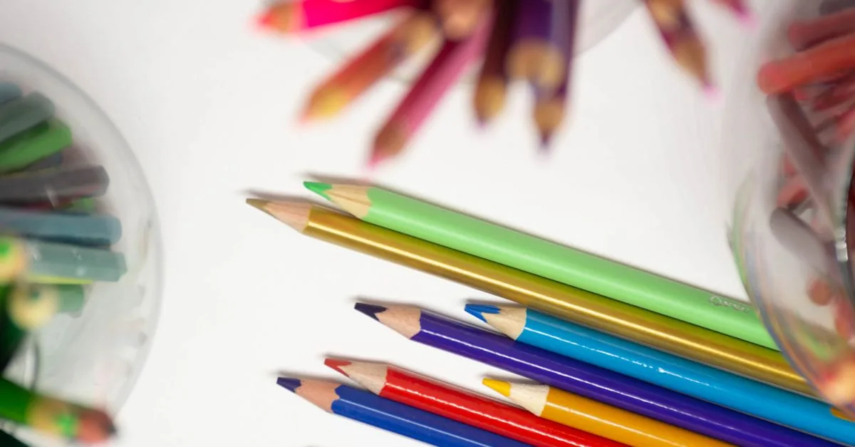 Frasco con monedas ahorradas junto a lápices de colores