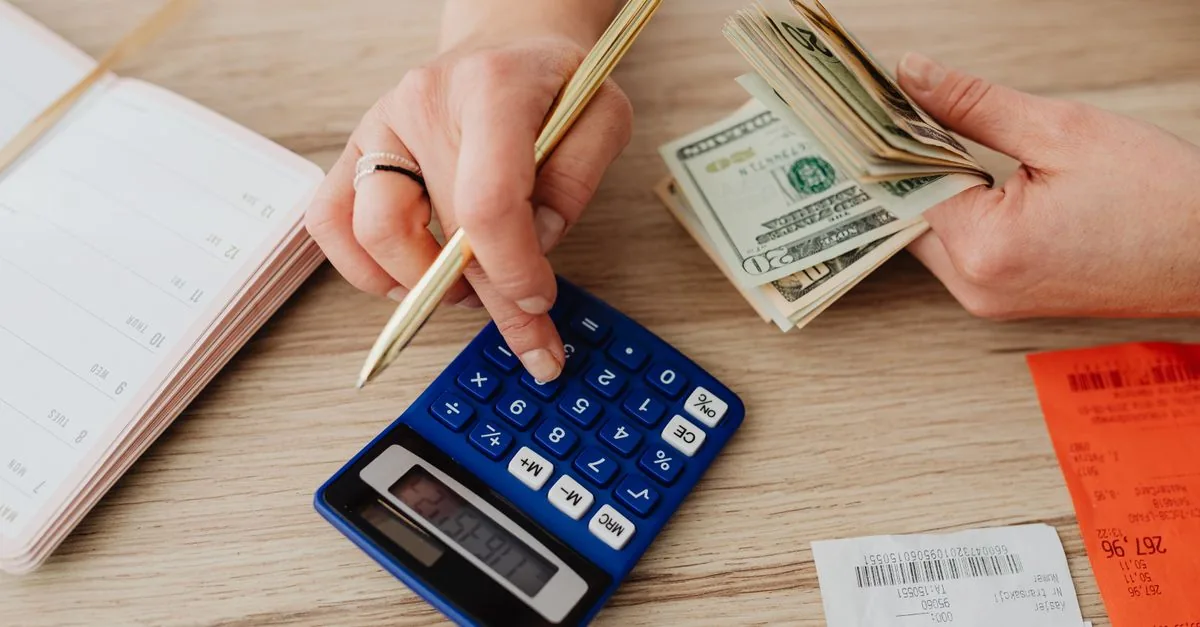 Persona recortando su lista de gastos con una calculadora al lado