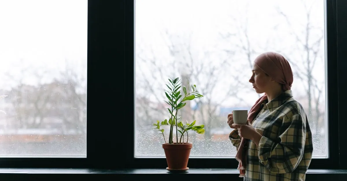 Persona pensativa frente a una ventana con una taza, reflexionando antes de comprar