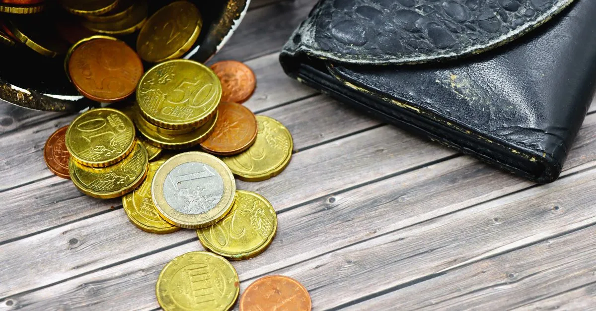 Cartera desgastada con monedas regadas sobre una mesa de madera