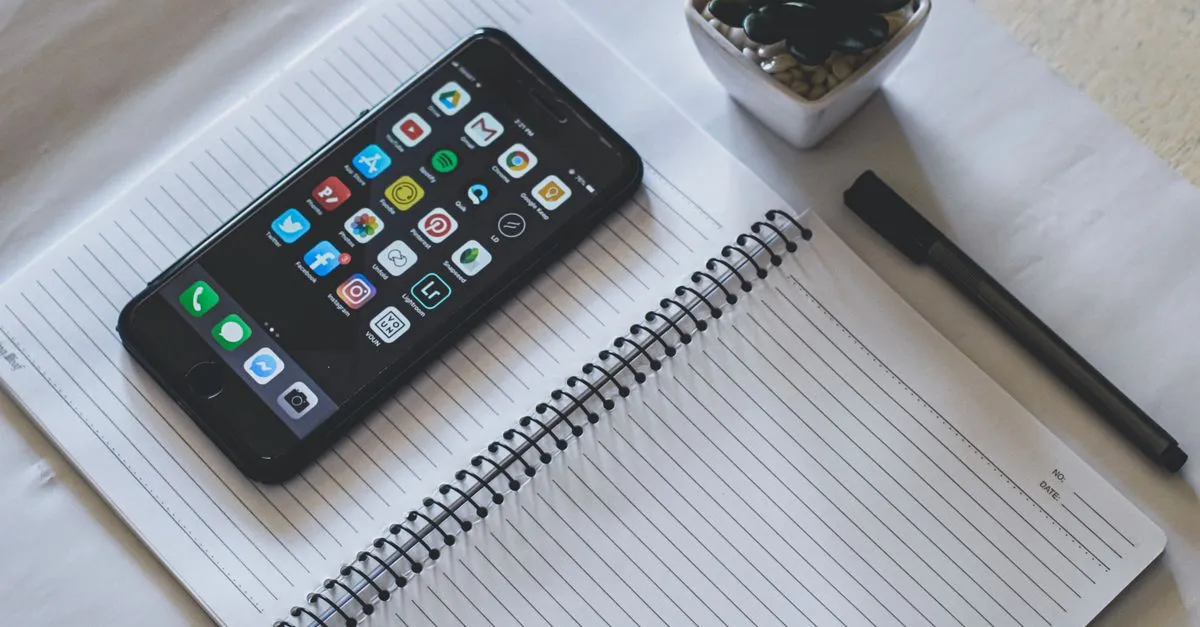 Celular con aplicaciones junto a una libreta en el escritorio