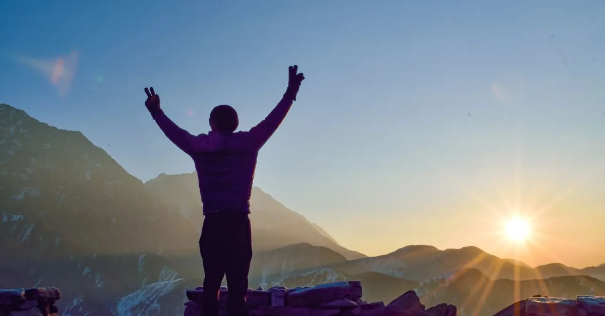 Persona con los brazos abiertos frente al amanecer en la montaña