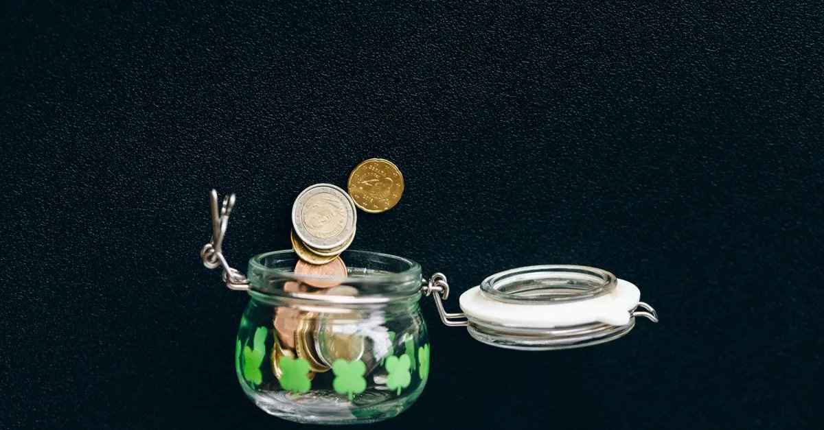 Monedas cayendo en un frasco de vidrio de ahorro