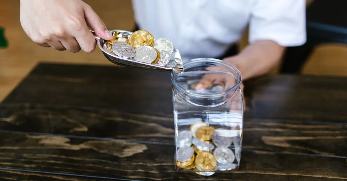 Mano guardando monedas en un frasco de vidrio de ahorro