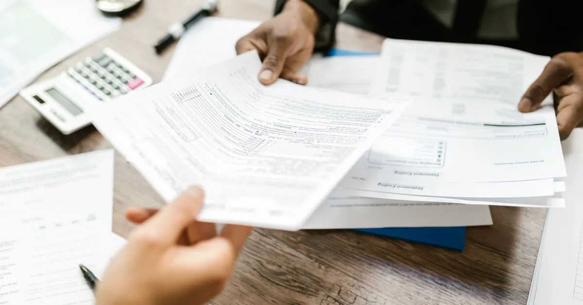 Manos revisando documentos y pólizas del año junto a una calculadora