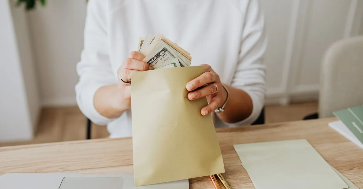 Mano apartando billetes en un sobre de ahorro el día de pago