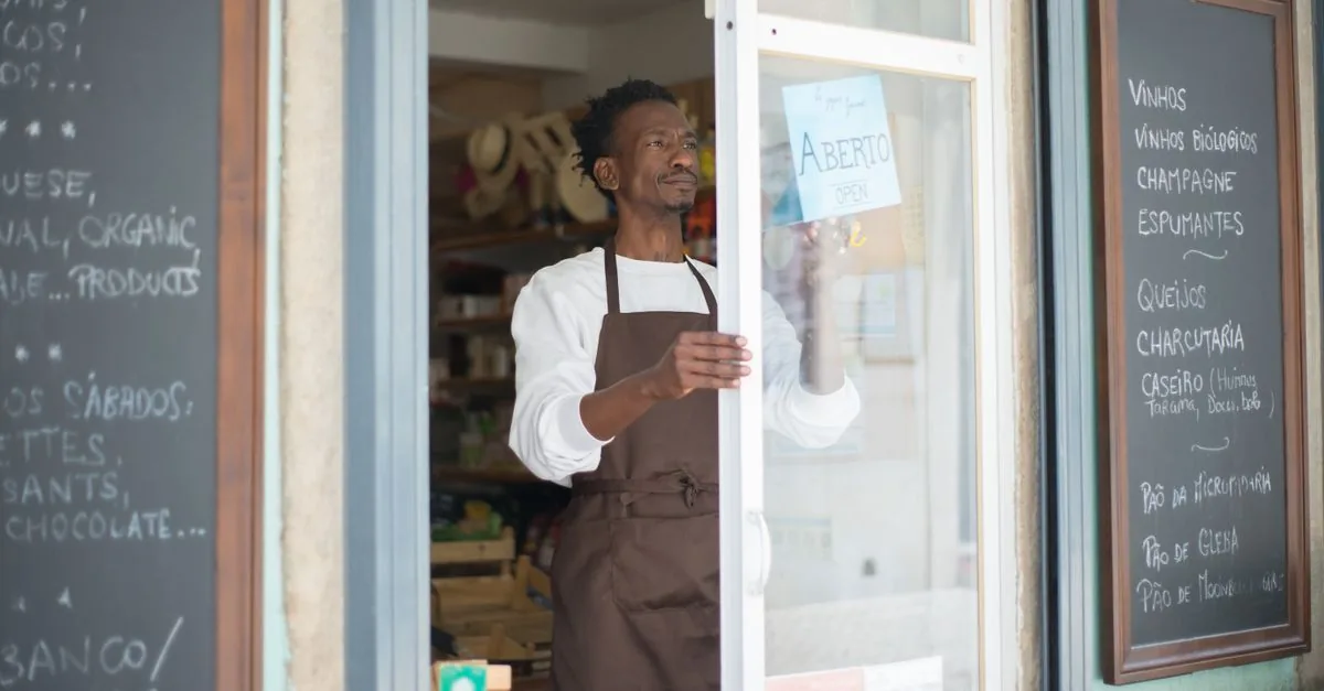 Comerciante en la puerta de su negocio con un letrero de abierto