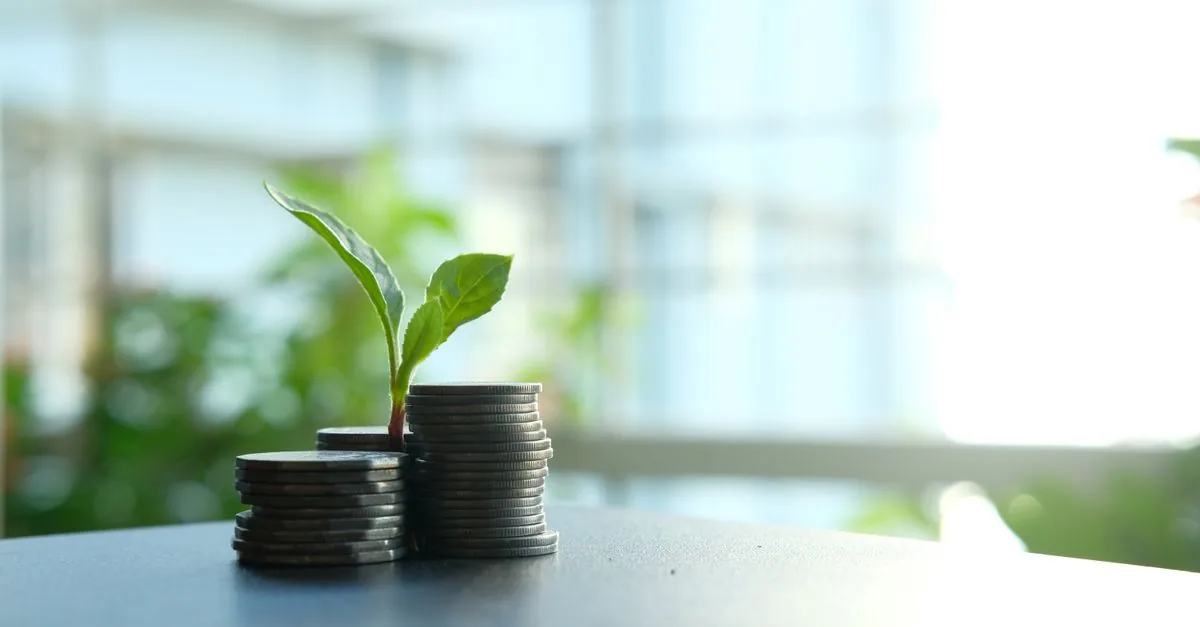 Monedas apiladas con una pequeña planta creciendo, símbolo del interés compuesto
