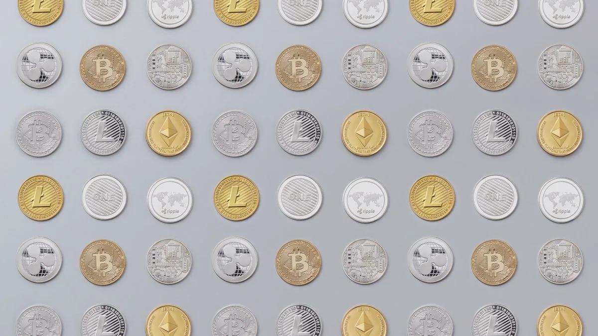 Monedas físicas de distintas criptomonedas (Bitcoin, Ethereum, Litecoin) ordenadas en filas sobre un fondo gris claro