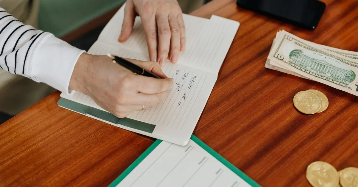 Persona anotando sus gastos del día en una libreta por la noche