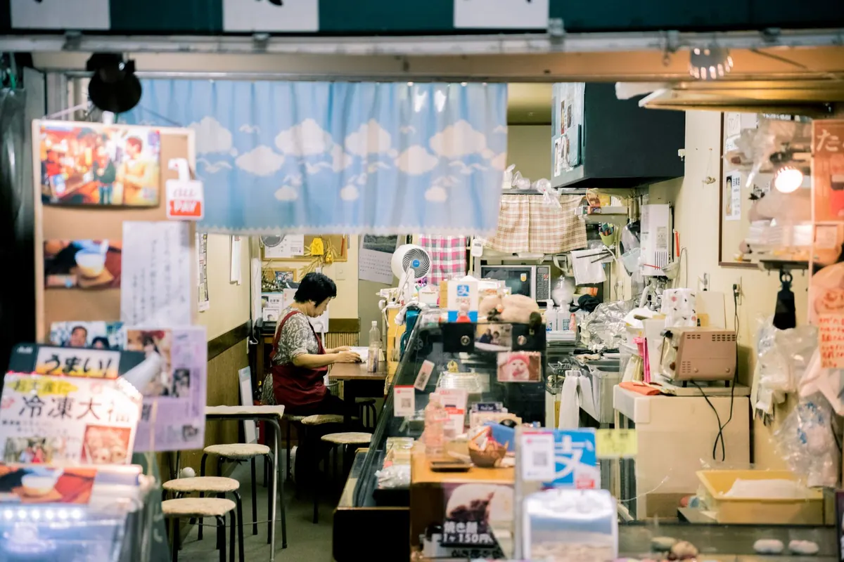 Dueña de una tienda pequeña revisando cuentas en un cuaderno junto al mostrador vacío